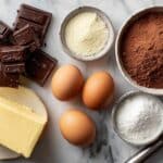 Składniki do klasycznego przepisu na brownie bez mąki ułożone na blacie, w tym gorzka czekolada i kakao.