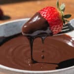 fondue czekoladowe z truskawką zanurzoną w płynnej czekoladzie