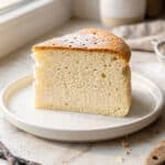Upieczony, wysoki i sernik puszysty jak chmurka oprószony cukrem pudrem, podany na jasnym blacie w estetycznej aranżacji kuchennej.